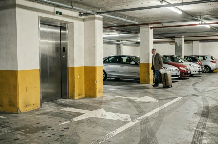 Intérieur d'un parking à plusieurs niveaux à Valence avec un homme tirant une valise vers l'ascenseur